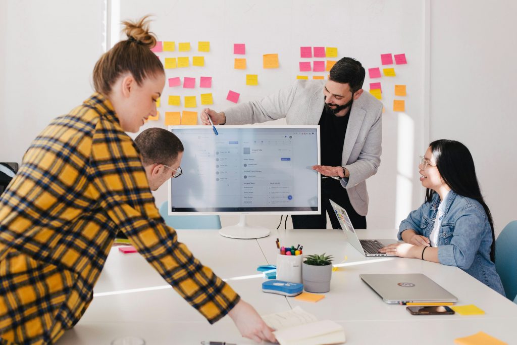 ein junges Team plant ein Projekt am Rechner in einem hellem Büro mit Infowand voller Post-Its