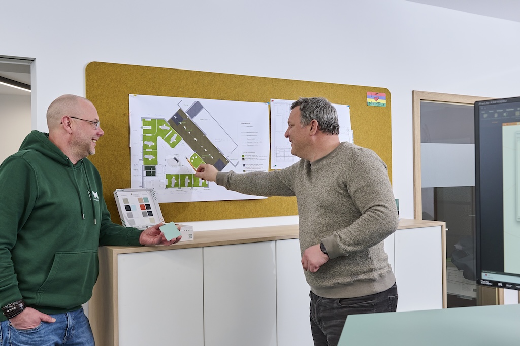 Zwei Architekten stehen an einem Plan, der an einer Pinwand hängt und besprechen ihr Projekt