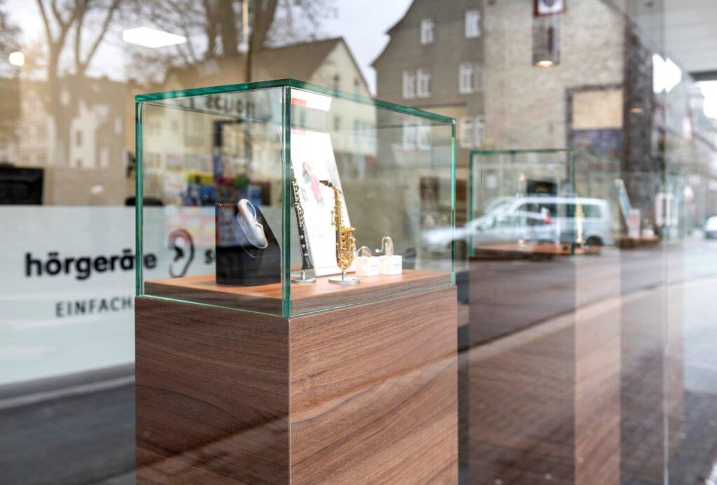 Glasvitrine im Schaufenster eines Hörakustikergeschäftes mit kleinem Saxophonmodell und Ohrmodell